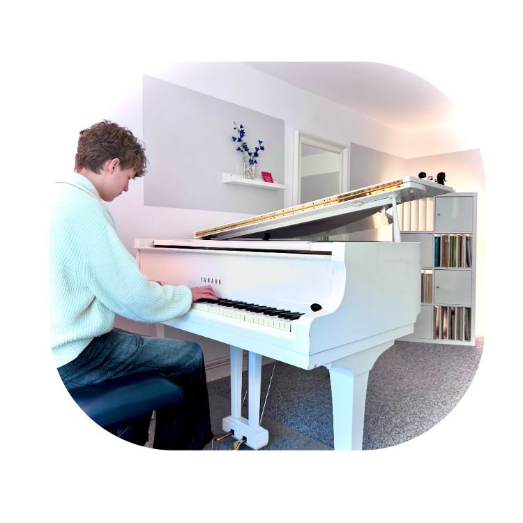 1. Bild Klavier Junger Mann sitzt an einem weißen Flügel mit dem Rücken zum Fotografen und spielt Klavier
