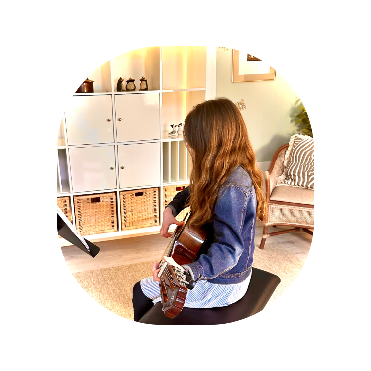 Mädchen sitz im Raum und spielt auf einer Gitarre, man sieht sie von der Seite, ihre Haare fallen ihr ins Gesicht.